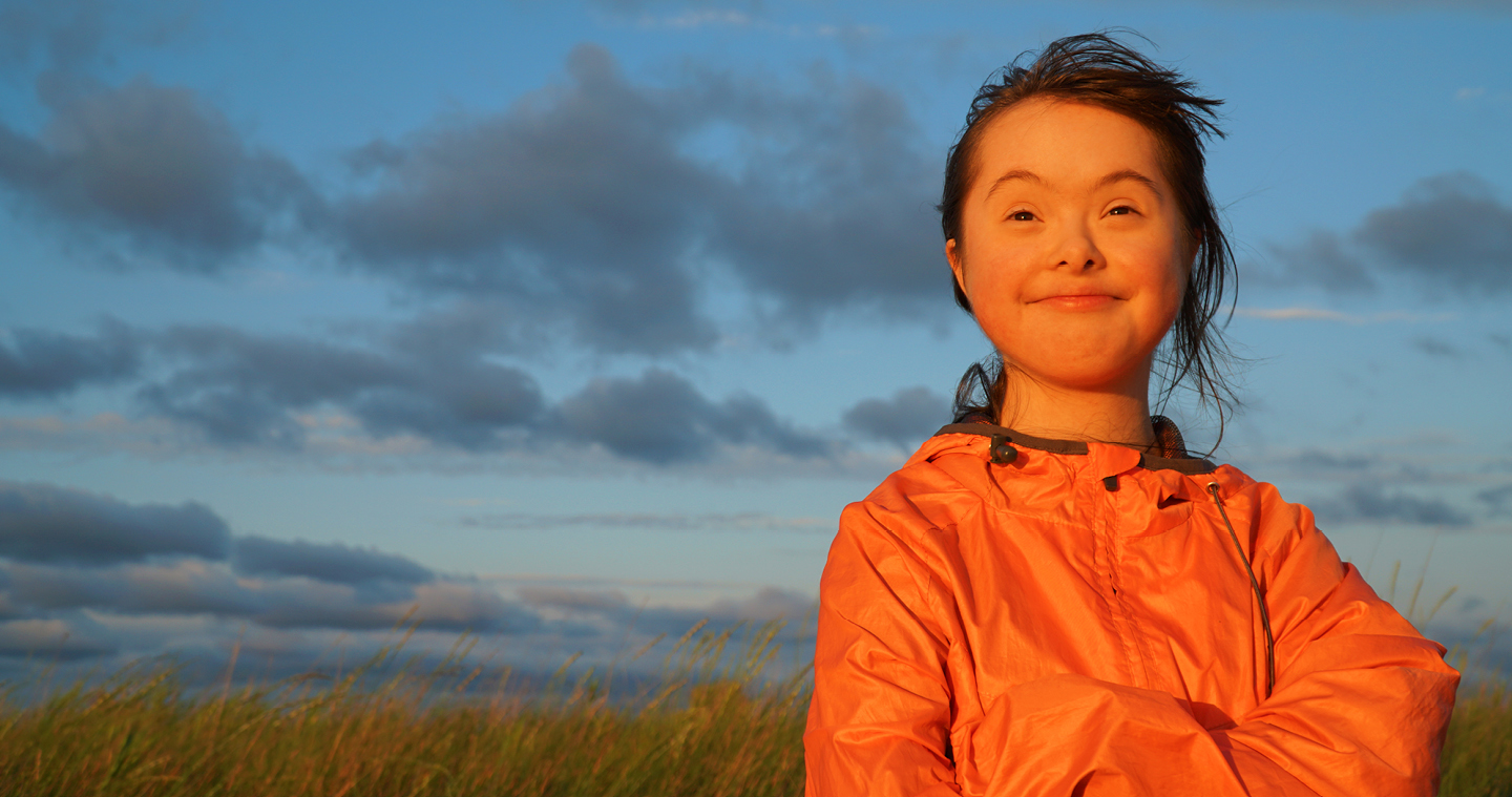 Child with Down Syndrome on a grassy field looking at the sunset